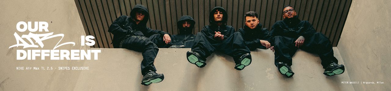 A young man in a black hooded tracksuit sits outdoors in front of tall apartment buildings, holding up a pair of black Nike Air Max TL 2.5 sneakers with green soles. The ad features bold white text reading “OUR AIR IS DIFFERENT” along with “NIKE Air Max TL 2.5 – SNIPES EXCLUSIVE.” At the bottom right