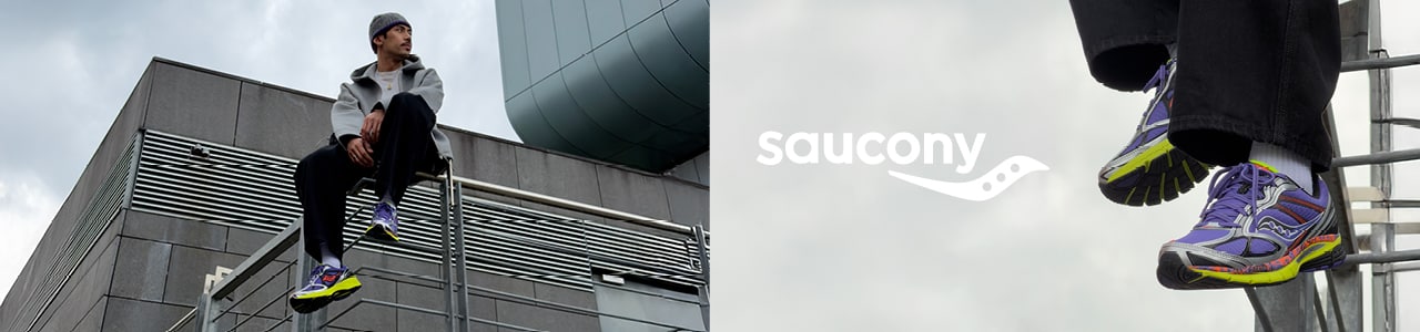 An outdoor lifestyle banner for Saucony featuring a person sitting on a metal railing of a modern, brutalist-style building under a cloudy sky.  On the left, the person is shown in a wide shot wearing a grey hoodie, dark trousers, a beanie, and vibrant purple and lime green Saucony sneakers. The center displays the Saucony logo in white against a grey, overcast sky. On the right, a close-up focuses on the person's feet dangling, highlighting the detailed design of the Saucony sneakers, which feature silver overlays and bright yellow soles.