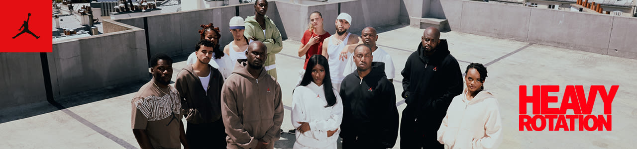 A promotional banner featuring three models standing on a grey concrete surface, viewed from a high angle. The model in the foreground adjusts a black hoodie, while the two models behind wear a brown track suit and a white hoodie. The top-left corner includes a red square with a black Jordan Jumpman logo, and the bottom-right corner features bold red text reading "HEAVY ROTATION."