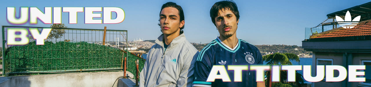 An promotional banner featuring five individuals posing outside a European-style cafe or storefront with a dark green facade. They are all wearing retro-style Adidas athletic apparel, including jerseys and jackets featuring the Germany national football team crest. On the left side of the banner, the text "UNITED BY" is displayed in a bold, white, stylized font with a soft neon glow. On the right side, the text "ATTITUDE" is written in the same font style, alongside a white Adidas Originals trefoil logo in the top right corner. The atmosphere is casual and relaxed, with the individuals sitting and standing around outdoor tables.