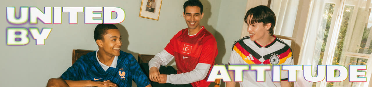 A promotional banner featuring five young individuals hanging out during a casual outdoor gathering in a backyard or patio setting. One person sits near a small charcoal grill with food cooking on it, while the others are seated around a patio table with food and drinks. They are all wearing different national football team jerseys, including France, Italy, Brazil, and Argentina. Large, stylized text overlays the image, with "UNITED BY" in the top-left corner and "ATTITUDE" across the bottom right, both featuring a bold white font with a soft neon glow.