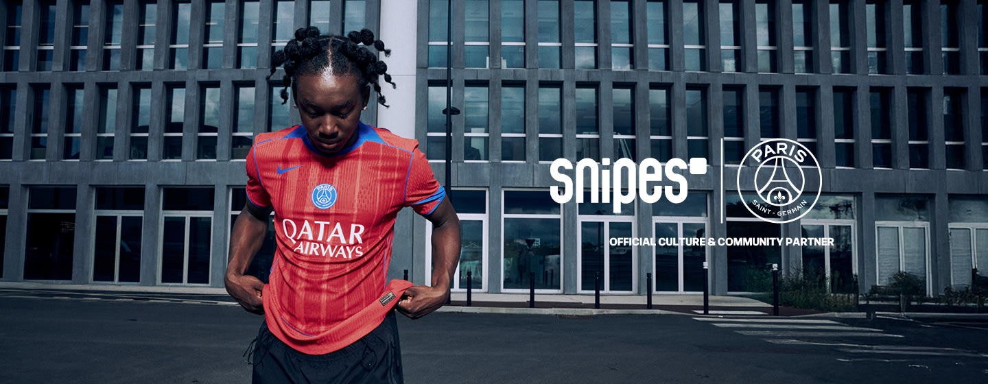 Model standing in front of urban building wearing a red football jersey from the PSG 3rd kit