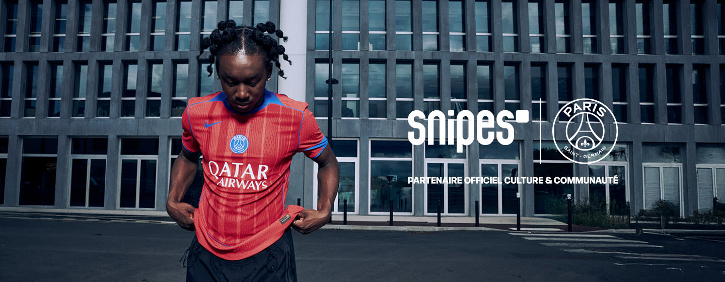 Model standing in front of urban building wearing a red football jersey from the PSG 3rd kit