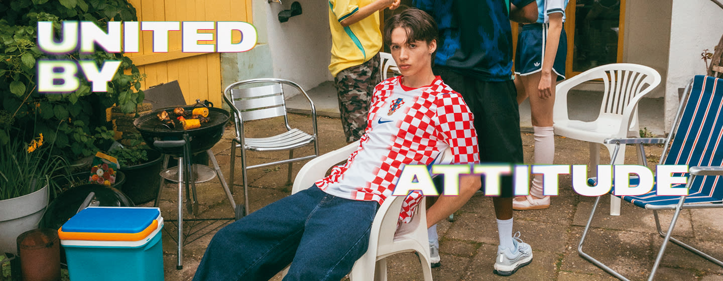 A promotional banner featuring five young individuals hanging out during a casual outdoor gathering in a backyard or patio setting. One person sits near a small charcoal grill with food cooking on it, while the others are seated around a patio table with food and drinks. They are all wearing different national football team jerseys, including France, Italy, Brazil, and Argentina. Large, stylized text overlays the image, with "UNITED BY" in the top-left corner and "ATTITUDE" across the bottom right, both featuring a bold white font with a soft neon glow.