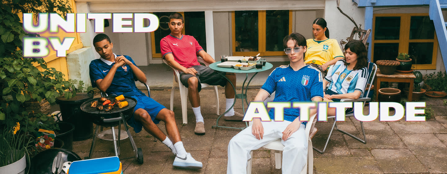 A promotional banner featuring five young individuals hanging out during a casual outdoor gathering in a backyard or patio setting. One person sits near a small charcoal grill with food cooking on it, while the others are seated around a patio table with food and drinks. They are all wearing different national football team jerseys, including France, Italy, Brazil, and Argentina. Large, stylized text overlays the image, with "UNITED BY" in the top-left corner and "ATTITUDE" across the bottom right, both featuring a bold white font with a soft neon glow.