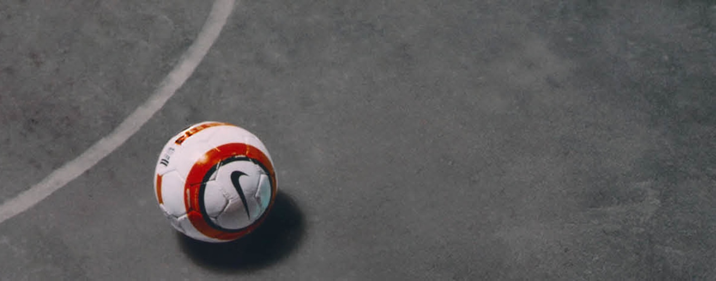 Image of a Nike white, red and black football ball laying on a grey court