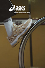 A close-up, wide-angle shot of a person’s feet on stone steps, wearing light grey and beige Asics GEL-NYC sneakers with white Snipes-branded crew socks. The Asics logo and the slogan "sound mind, sound body" are displayed in white on the left side.