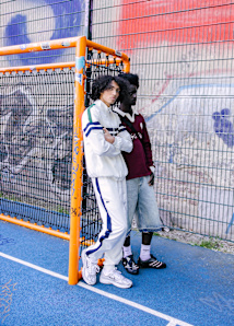 2 young men on concrete football field leaning against the goal and wearing tracksuits and other sporty styles