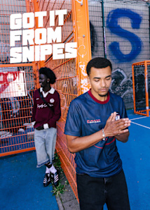 Two young men are sitting on a bright blue outdoor sports court in front of a fence and graffiti-covered wall. They are dressed in casual streetwear clothing, including track pants, jackets, and sneakers. Large bold white text above them reads, “GOT IT FROM SNIPES.”