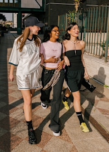 group of young women walking down the street smiling and holding hands. They wear summer festival streetwear.
