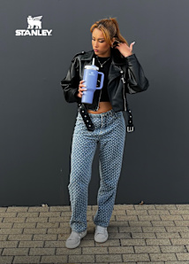 Female model wearing leather jacket and blue jeans while holding a blue Stanley cup