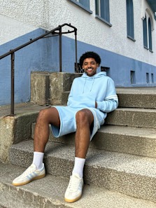 Guy sitting outside in the stairs with a light blue adidas hoodie and shorts smiling