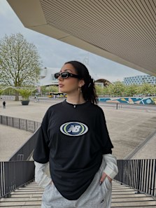 Woman standing on stairs wearing black new balance t-shirt with white longsleeve t-shirt underneath