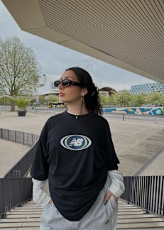 Woman standing on stairs wearing black new balance t-shirt with white longsleeve t-shirt underneath