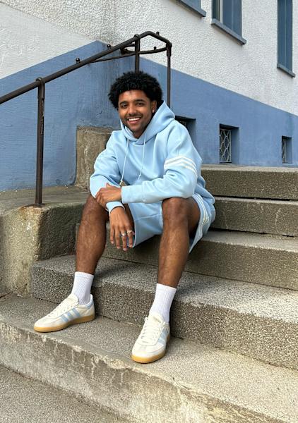 Guy sitting in the stairs wearing a hoodie and pants from adidas and adidas shoes 