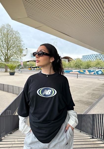 Girl in stairs wearing a black tshirt from new balance with a layered white long sleeve shirt underneath 