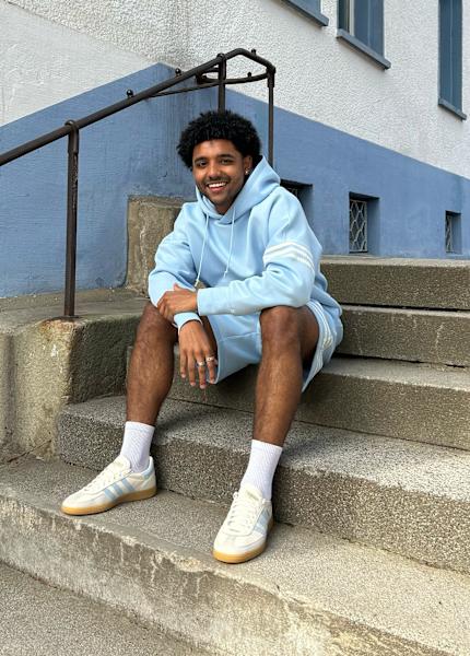 Guy sitting in the stairs wearing a hoodie and pants from adidas and adidas shoes 
