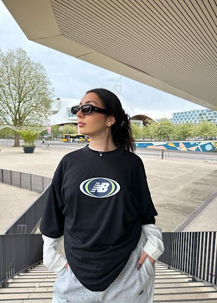 Girl in stairs wearing a black tshirt from new balance with a layered white long sleeve shirt underneath 