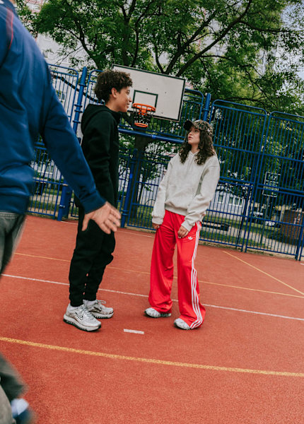 A group of teenagers wearing casual sportswear, including Adidas clothing, hanging out in an urban outdoor setting.