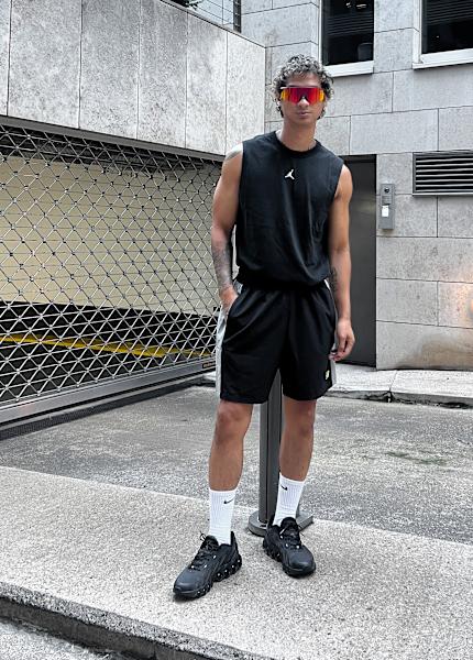 Male model wearing black outfit in running style aesthetics: black running shoes, shorts and tanktop with colorful sunglasses.