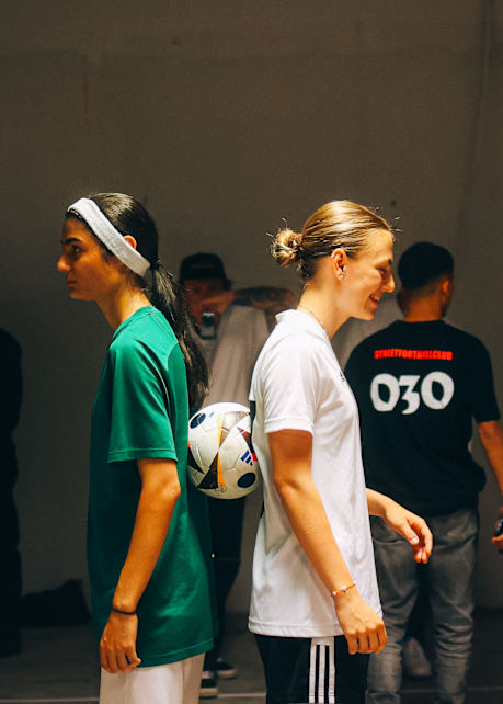 snipes serves event 2 girls at a street football competition standing back to back with a football in between them
