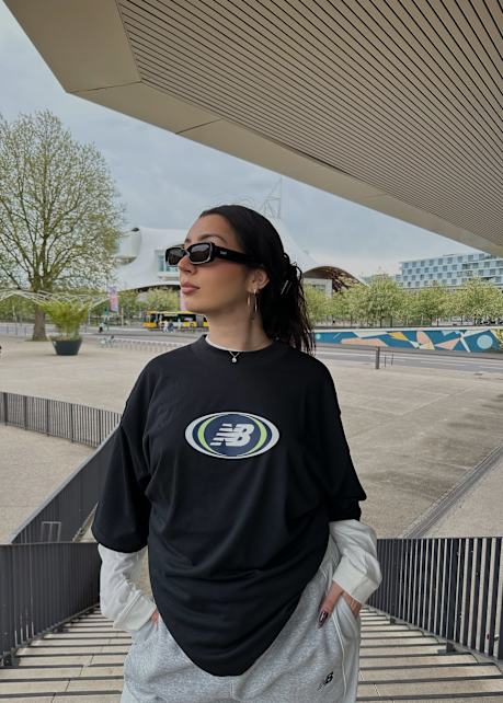 Woman standing on stairs wearing black new balance t-shirt with white longsleeve t-shirt underneath