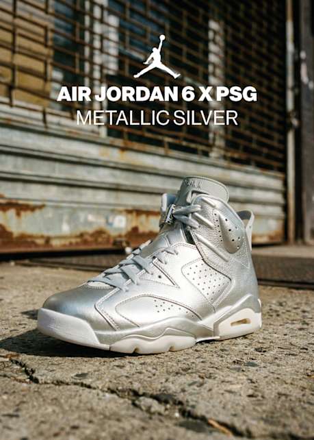 A pair of high-top Air Jordan 6 x PSG sneakers in 'Metallic Silver' featuring a shimmering silver leather upper, white laces, and translucent soles. The shoes are pictured on a city sidewalk against an urban backdrop, accompanied by a white Jumpman logo and text identifying the model.