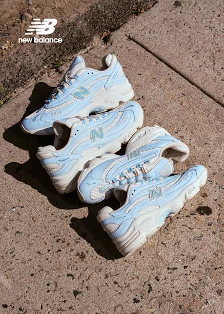 New Balance Sneakers light blue and white at the center of the image,laying on the street 