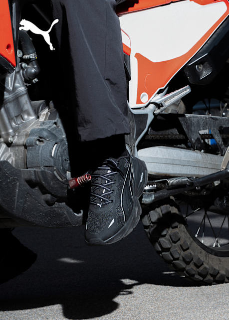 male model driving a motorcycle wearing a grey tracksuit and white Puma sneakers