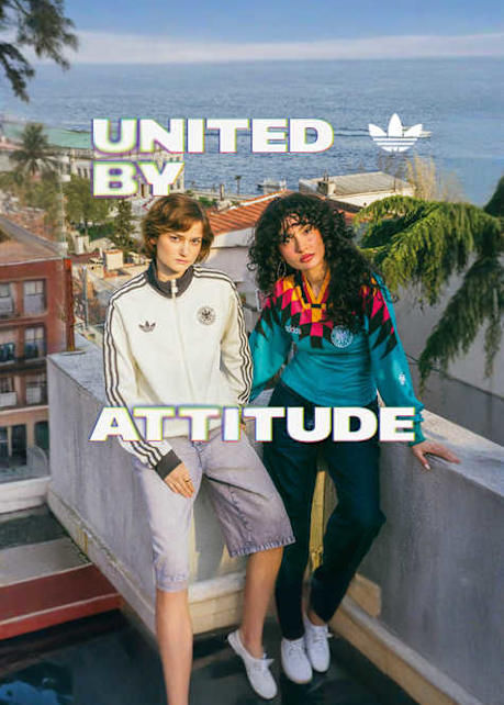 An promotional banner featuring five individuals posing outside a European-style cafe or storefront with a dark green facade. They are all wearing retro-style Adidas athletic apparel, including jerseys and jackets featuring the Germany national football team crest. On the left side of the banner, the text "UNITED BY" is displayed in a bold, white, stylized font with a soft neon glow. On the right side, the text "ATTITUDE" is written in the same font style, alongside a white Adidas Originals trefoil logo in the top right corner. The atmosphere is casual and relaxed, with the individuals sitting and standing around outdoor tables.