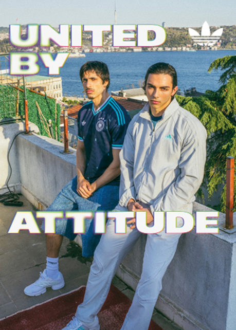 An promotional banner featuring five individuals posing outside a European-style cafe or storefront with a dark green facade. They are all wearing retro-style Adidas athletic apparel, including jerseys and jackets featuring the Germany national football team crest. On the left side of the banner, the text "UNITED BY" is displayed in a bold, white, stylized font with a soft neon glow. On the right side, the text "ATTITUDE" is written in the same font style, alongside a white Adidas Originals trefoil logo in the top right corner. The atmosphere is casual and relaxed, with the individuals sitting and standing around outdoor tables.