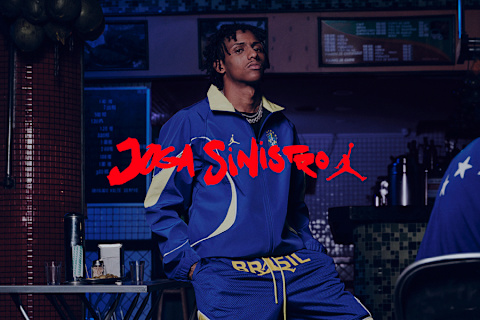 male model wearing Jordan x Brazil Football Collection: violet track jacket with yellow details, and sport shorts in same colors.