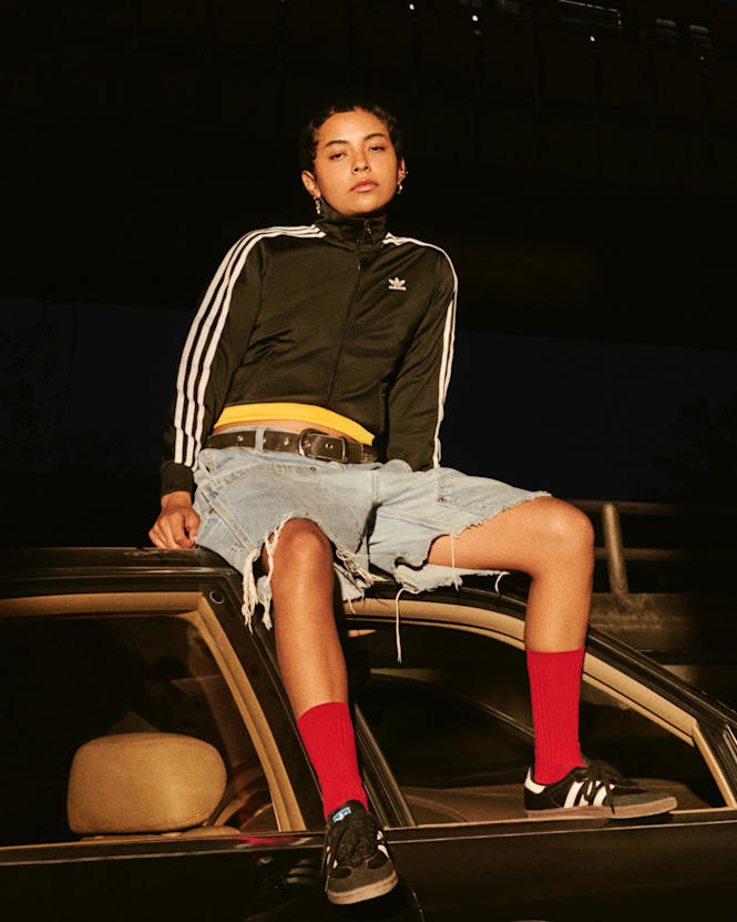 Model with Adidas Firebird Jacket and Jeans Shorts sitting on a car