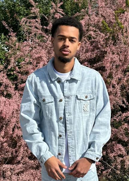 Guy wearing a light denim jacket with behind flowes