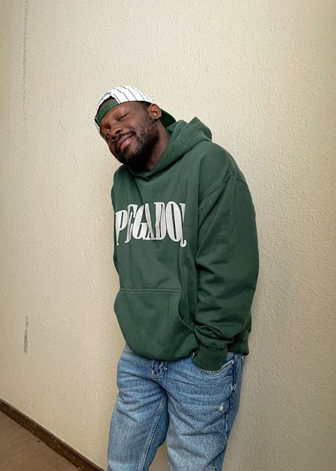 Guy wearing a green hoodie smiling with a white cap